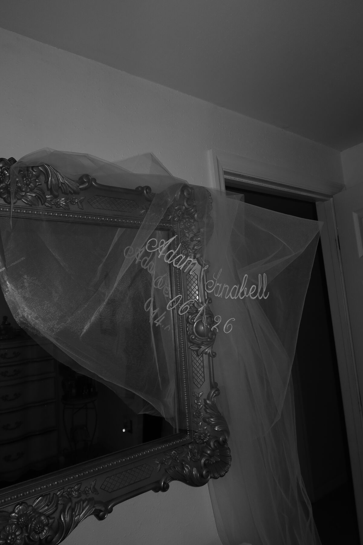 A veil draped over a carved mirror, two names and a wedding date embroidered across it.